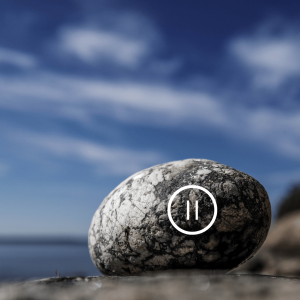 A rock with a pause symbol on it with the blue sky behind it. 